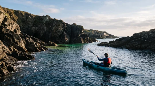 Kayakiste solitaire pagayant au ras de l'eau devant des falaises rocheuses et une crique cachée de la côte de Jade en Loire-Atlantique